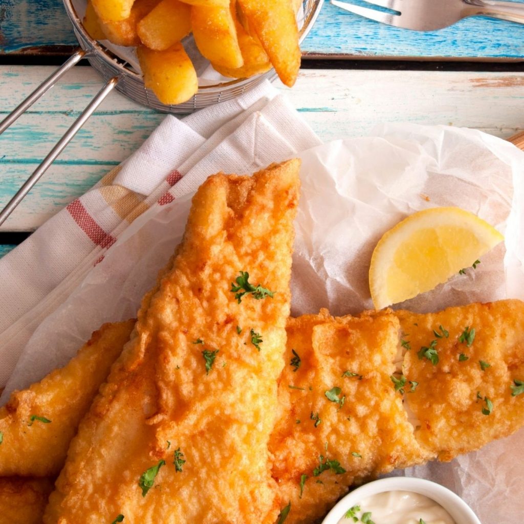A serving of fish and chips has a lemon wedge on the side.
