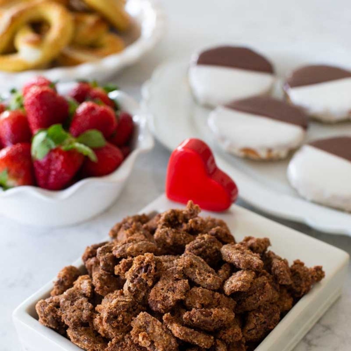 A variety of New York themed party foods are on the kitchen counter including a container of sugared nuts, black and white cookies, fresh strawberries.