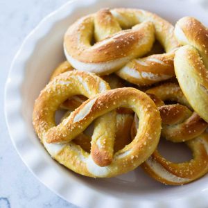 A pie plate holds a pile of baked fluffy pretzels with chunks of kosher salt sprinkled over the top.