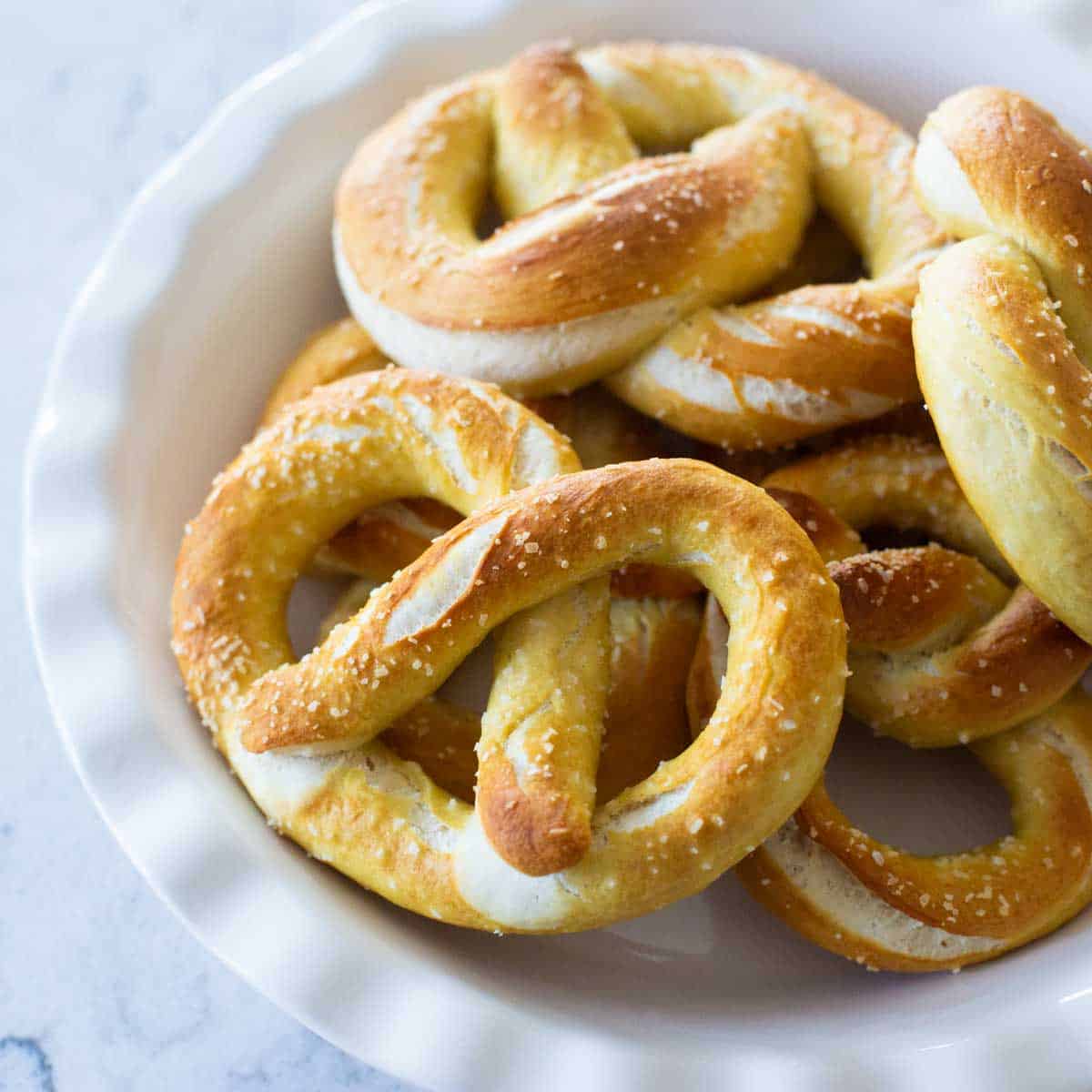 A pie plate holds a pile of baked fluffy pretzels with chunks of kosher salt sprinkled over the top.