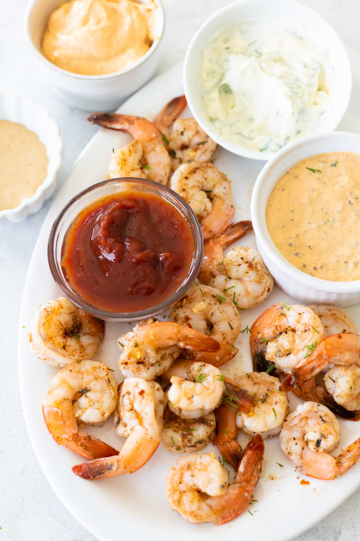 A platter of shrimp has several cups of dip on the platter.