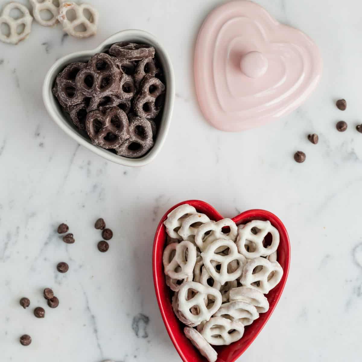 2 heart-shaped bowls are filled with chocolate covered pretzels.