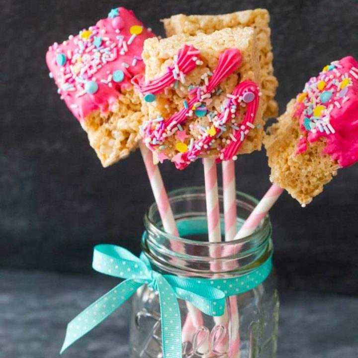 A jar full of rice crispie bar pops with pink icing and sprinkles.