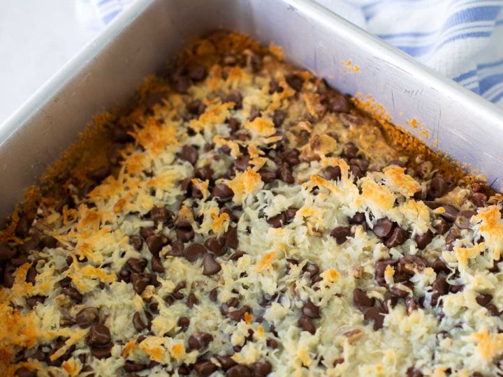 A metal baking pan is filled with hello dolly bars topped with shredded coconut and chocolate chips.