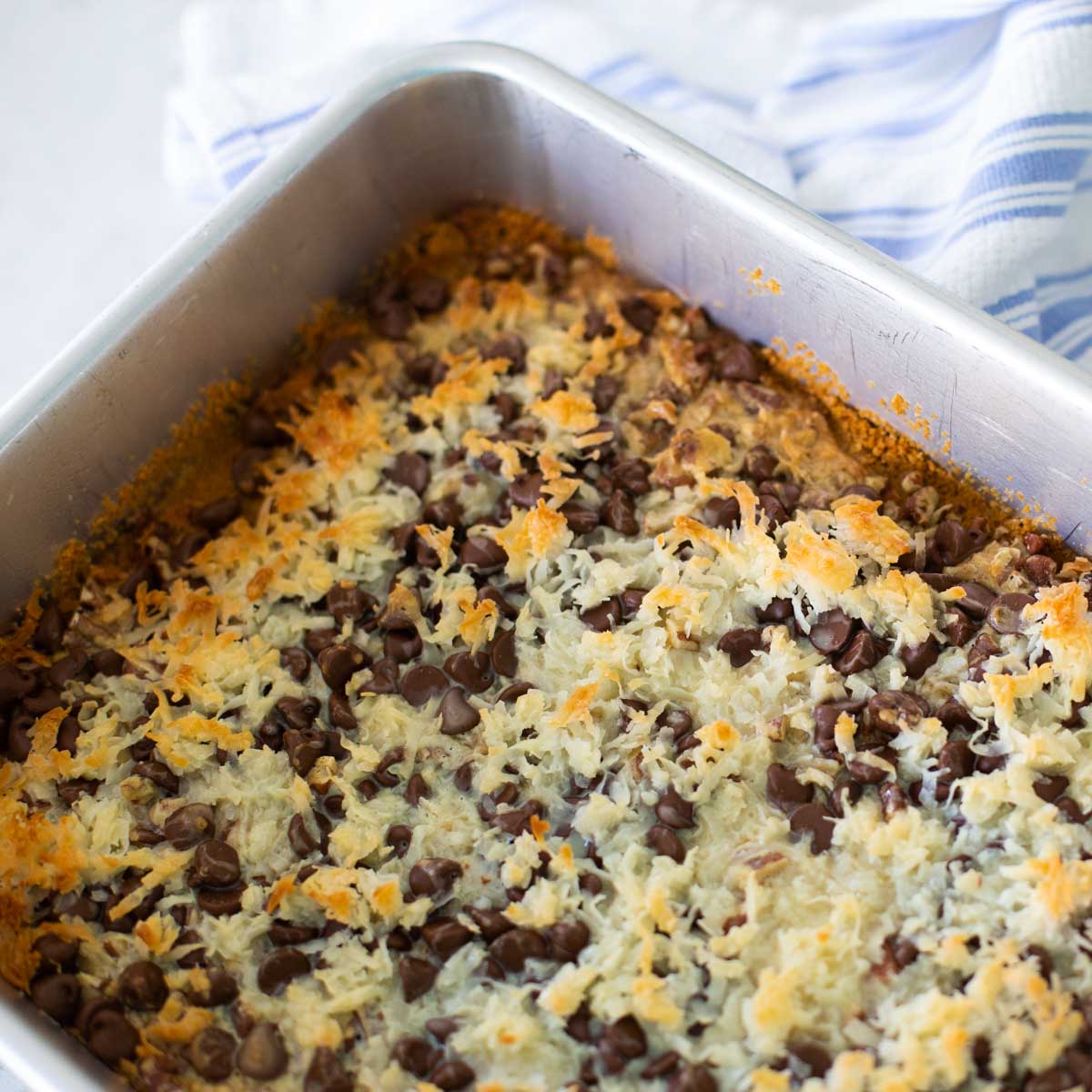 A metal baking pan is filled with hello dolly bars topped with shredded coconut and chocolate chips.