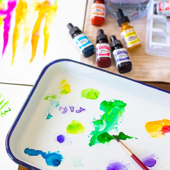 A butcher tray filled with watercolor paints sits on a table next to several bottles of paint.