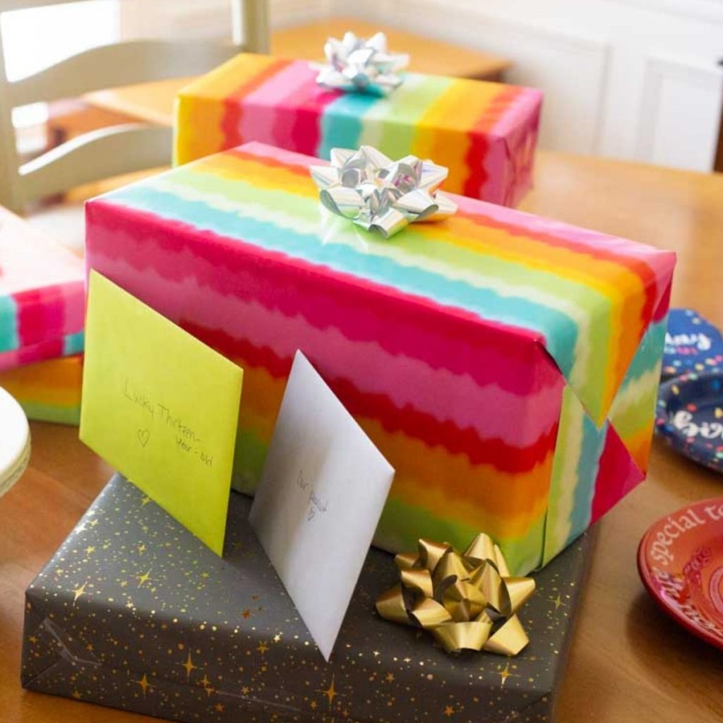 Tie dye wrapping paper birthday gifts with cards sit on a table.