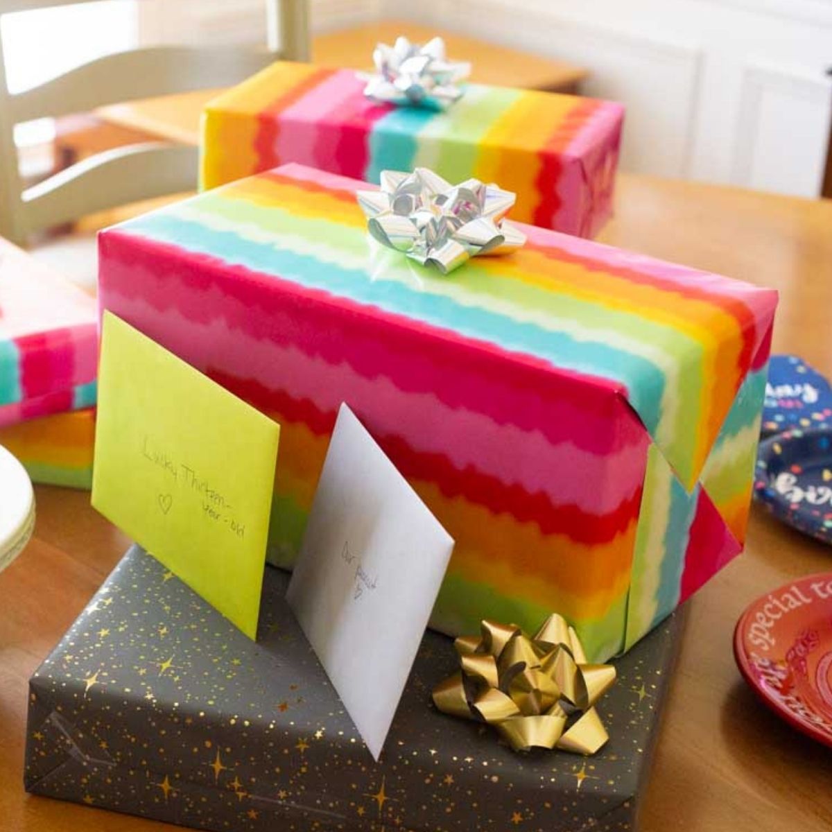 Tie dye wrapping paper birthday gifts with cards sit on a table.