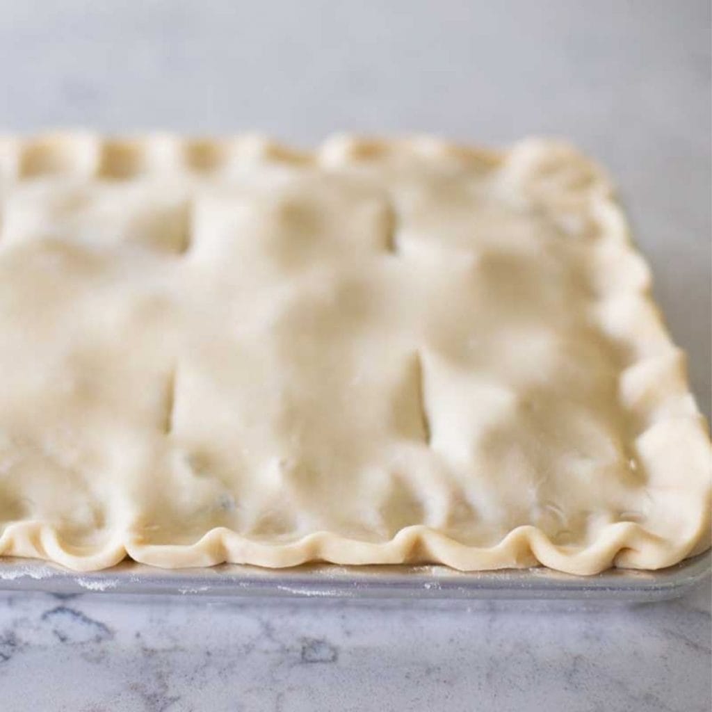 An all-butter pie crust dough has been assembled in a baking pan with a ruffled edge.