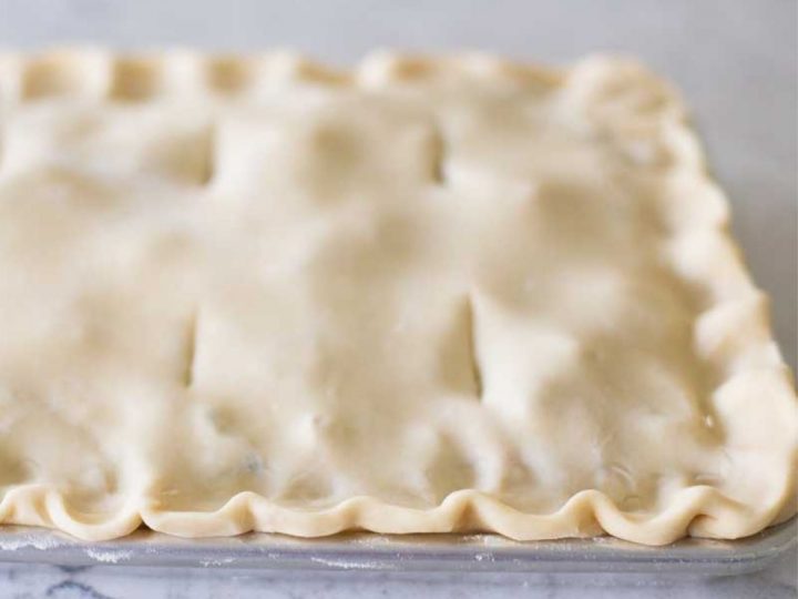An all-butter pie crust dough has been assembled in a baking pan with a ruffled edge.