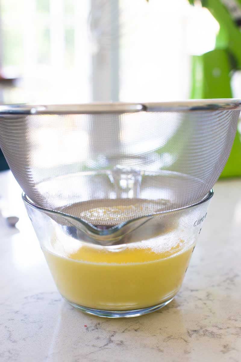 A large strainer is set over a large measuring cup, the creme anglaise has been poured through.