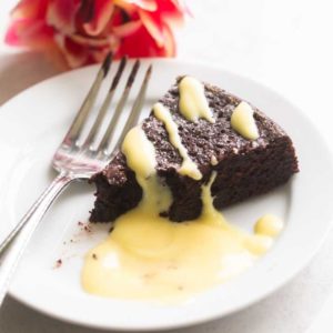 Creme anglaise, a rich custard sauce has been drizzled over a slice of chocolate flourless torte. A fork is scooping a bite.