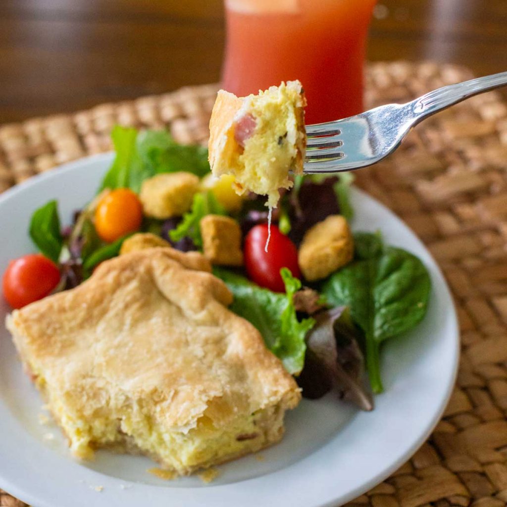 The eggs and ham slab pie has been sliced and served on a plate next to a small green salad.
