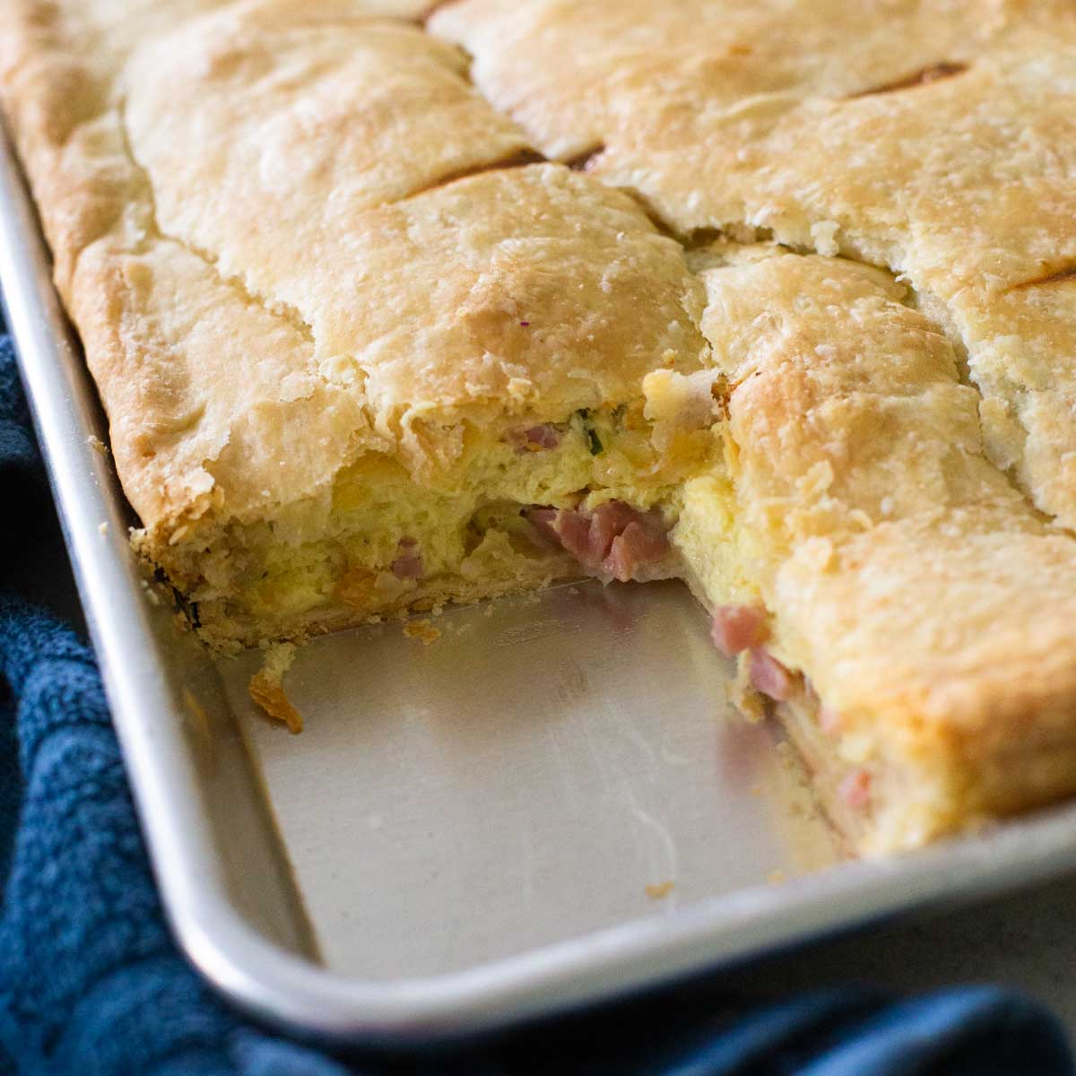 A metal baking pan has an egg and ham breakfast pie with a buttery, flaky pie crust.