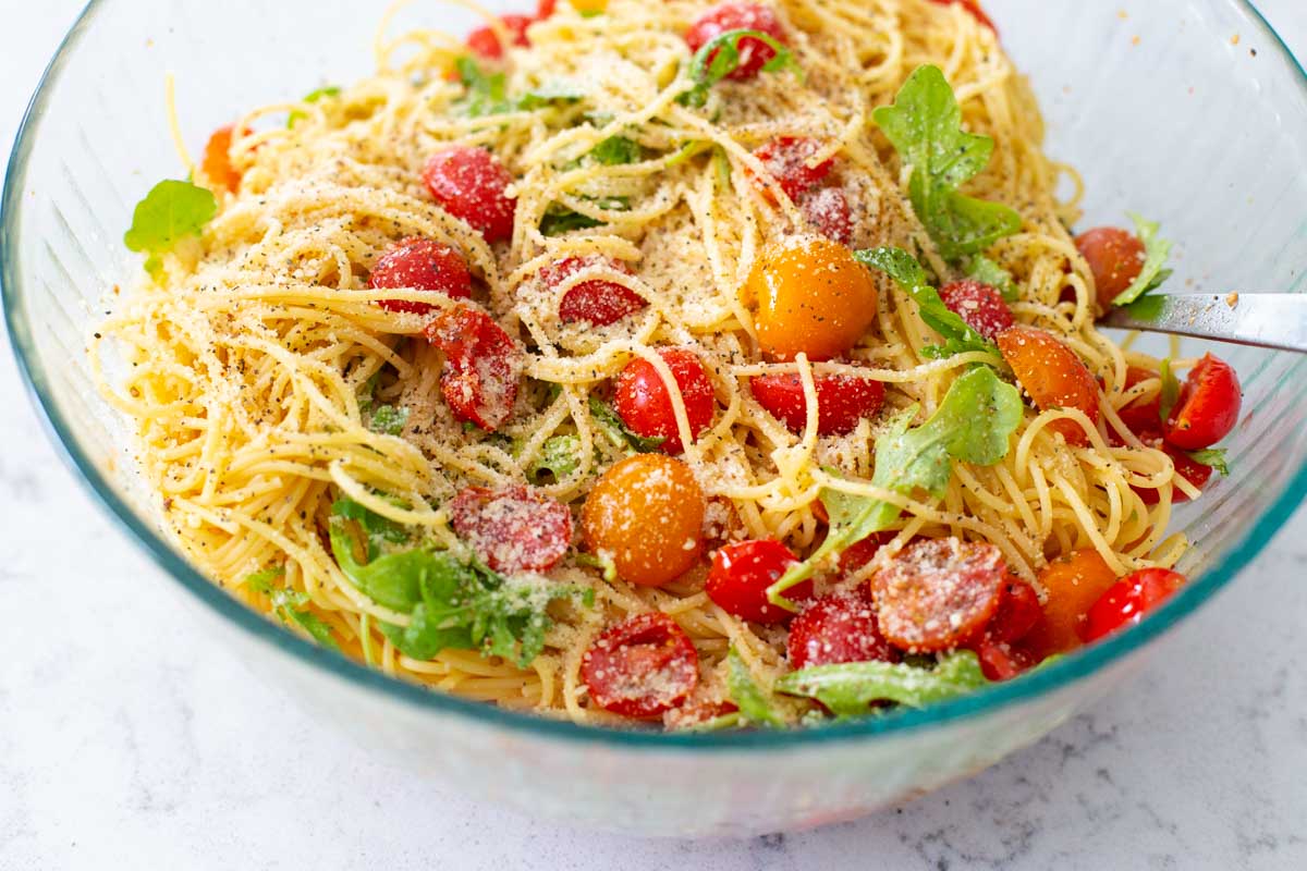 A large mixing bowl has the pasta and fresh tomatoes tossed together.