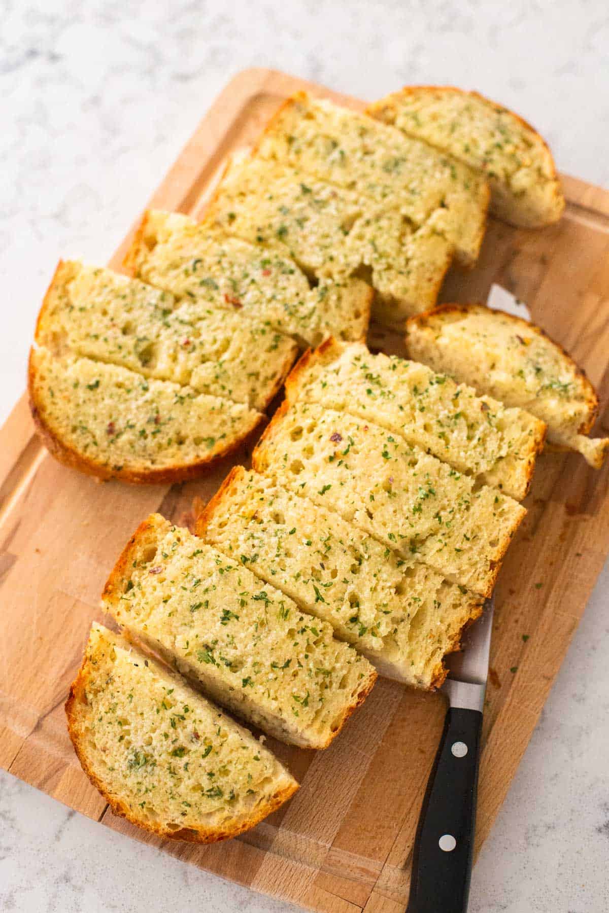 The baked garlic bread is on a cutting board and has been cut into wedges for serving.