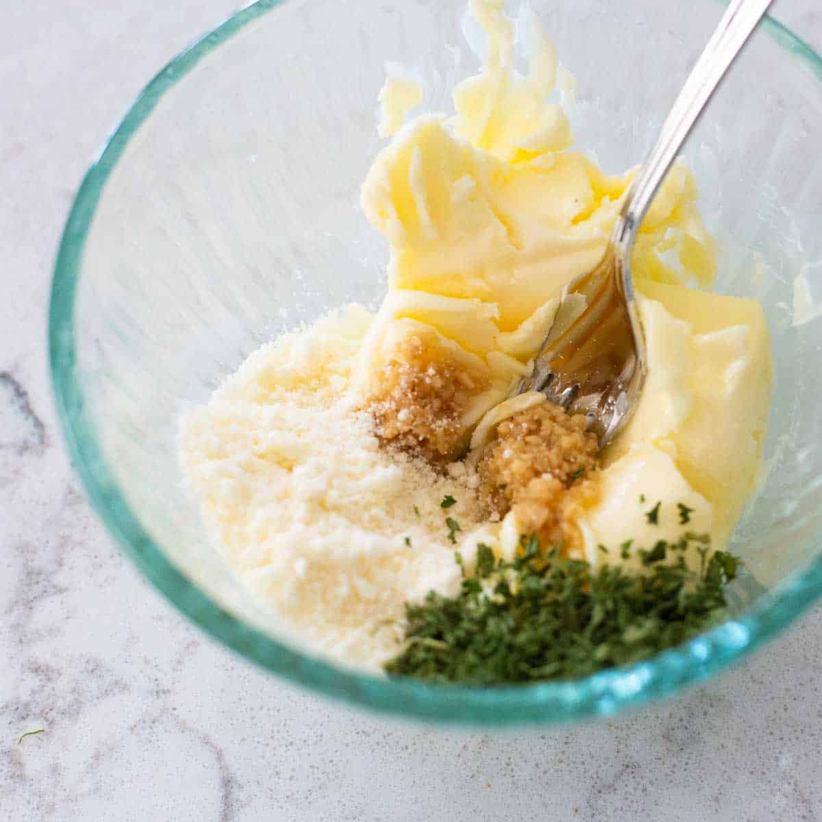 A small mixing bowl has the ingredients for the garlic bread ready to be mixed.