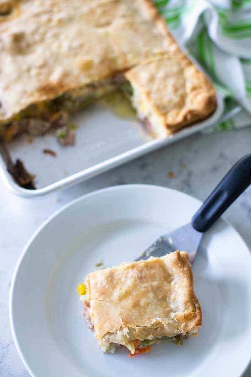 A square slice of ham pot pie is served on a white plate.