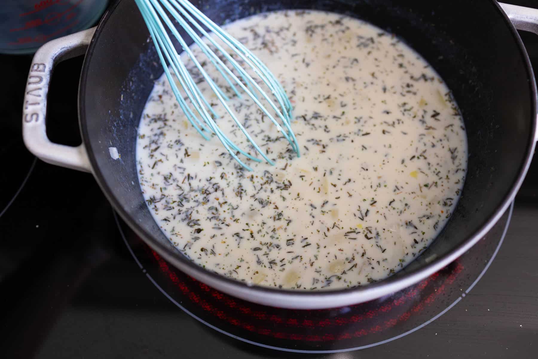 The milk has been added to the pan and is now being whisked in to thicken.