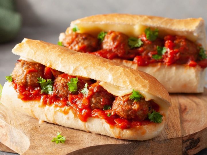 A pair of meatball sub sandwiches are on a cutting board for serving.