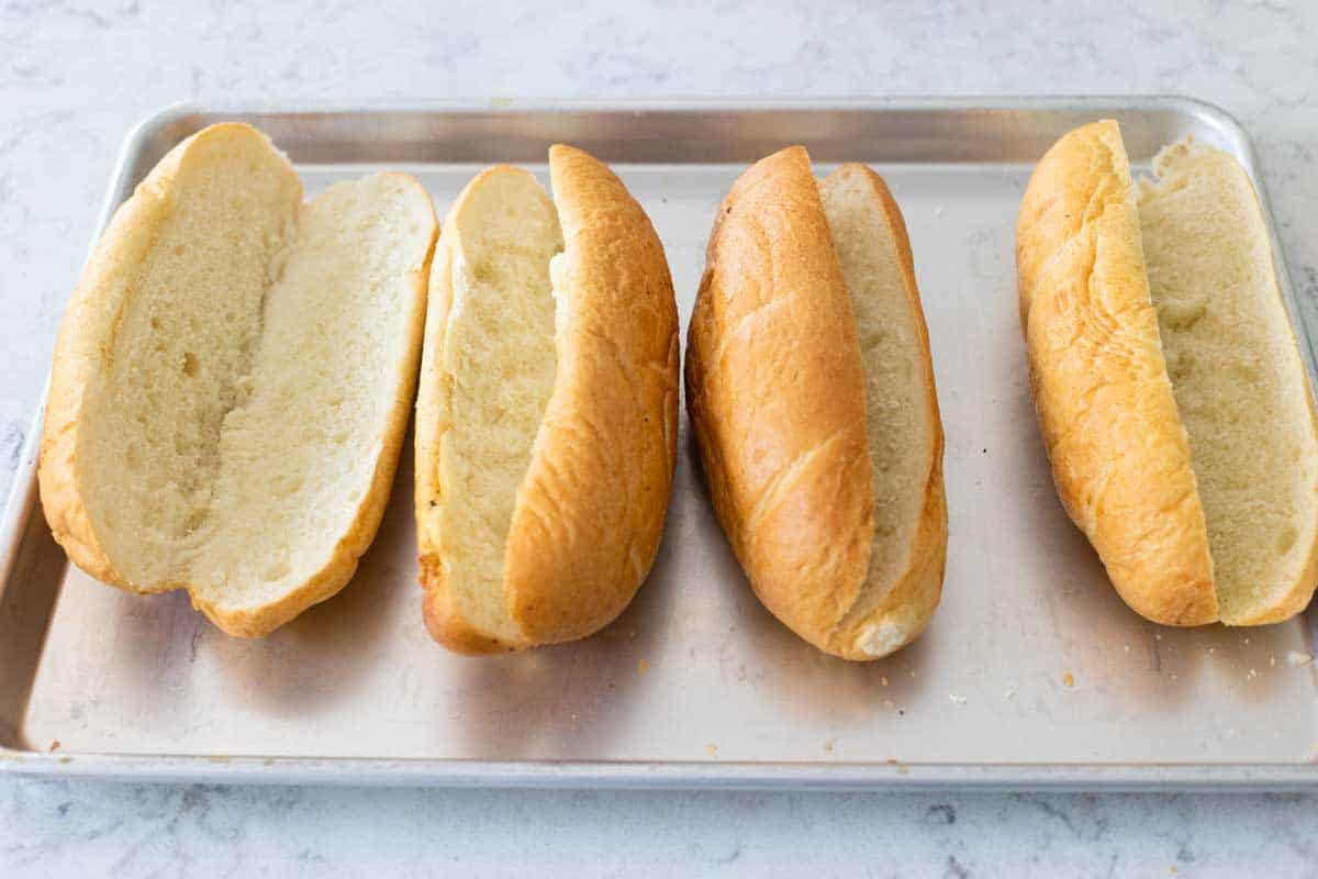 The sub rolls have been split open and laid on a sheet pan.