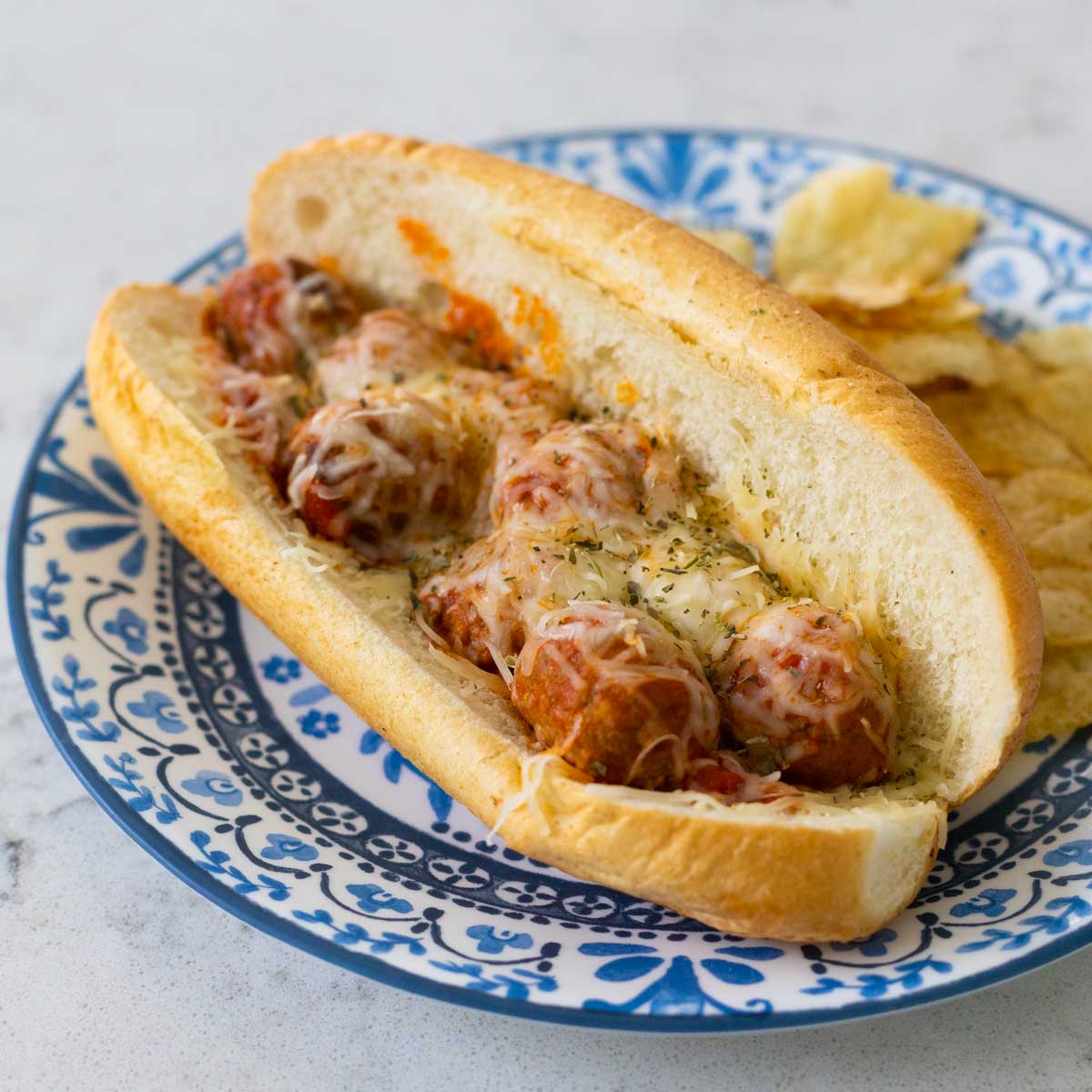 A blue plate has a long baked meatball sub with tomato sauce and melted cheese.