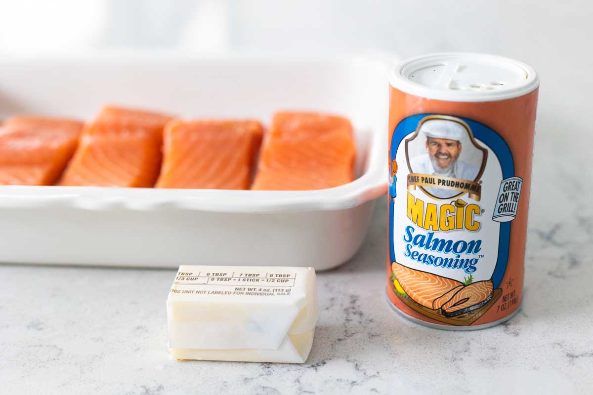 The baking pan of salmon is next to a bottle of seasoning and a stick of butter.