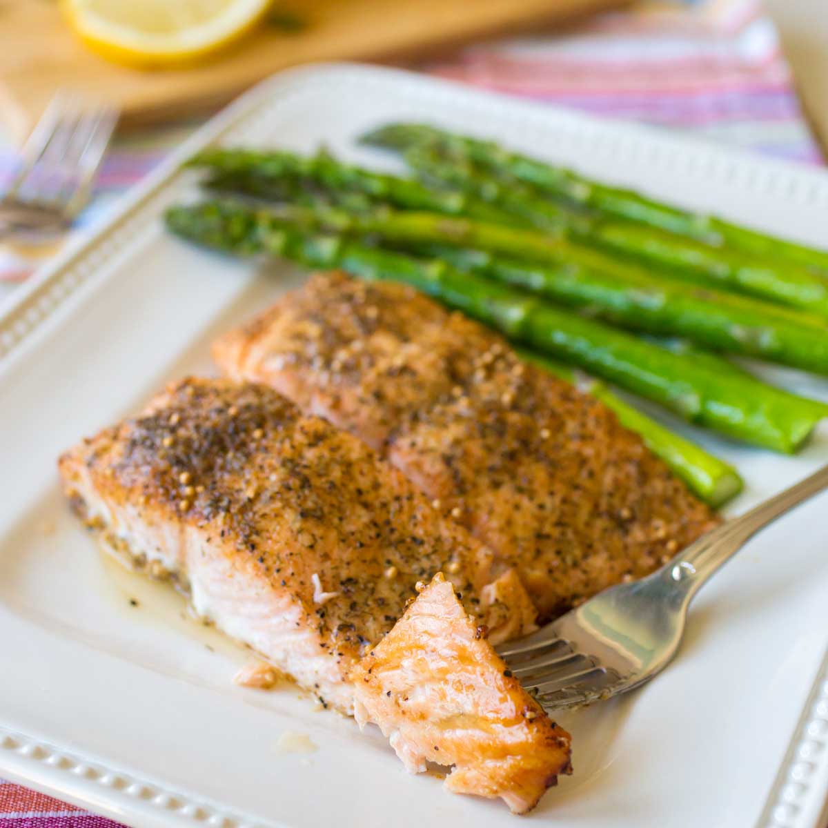A platter of oven baked salmon next to roasted asparagus has a fork showing the flaky pink fish.