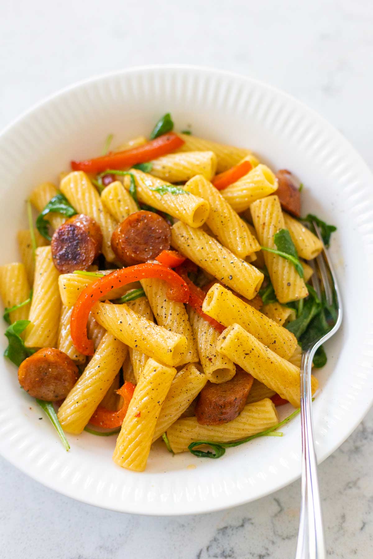 The sausage and peppers pasta is in a white bowl with a fork.