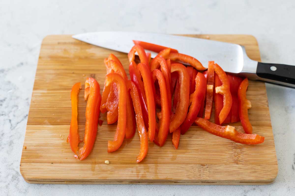 The red bell pepper has been thinly sliced on the cutting board.