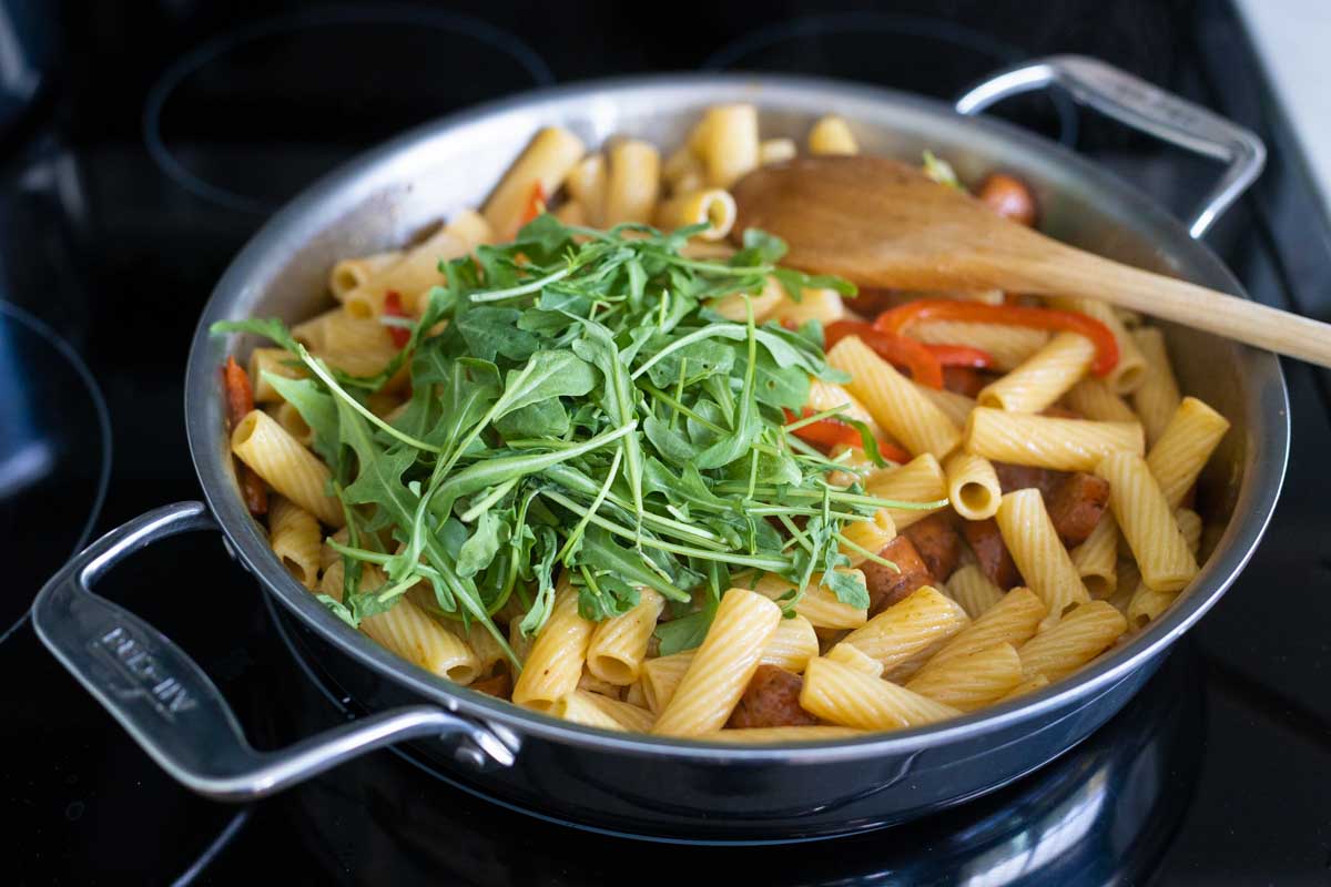The cup of arugula has been added to the skillet.
