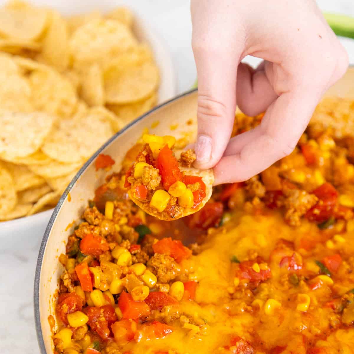 A young girl's hand dips a tortilla chip into the taco skillet.