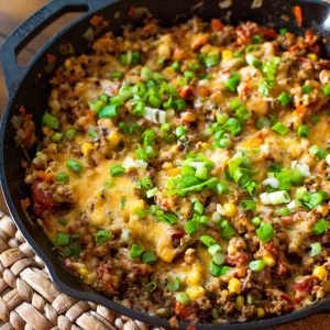 A cast iron skillet holds ground turkey taco skillet with melted cheese and fresh green onions sprinkled over the top.