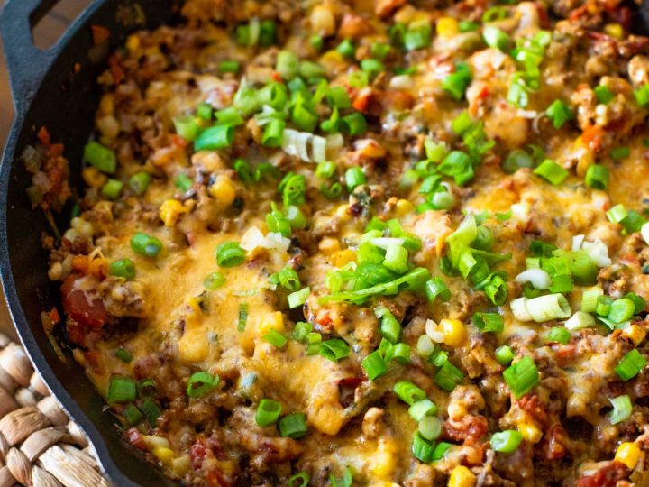 A cast iron skillet holds ground turkey taco skillet with melted cheese and fresh green onions sprinkled over the top.