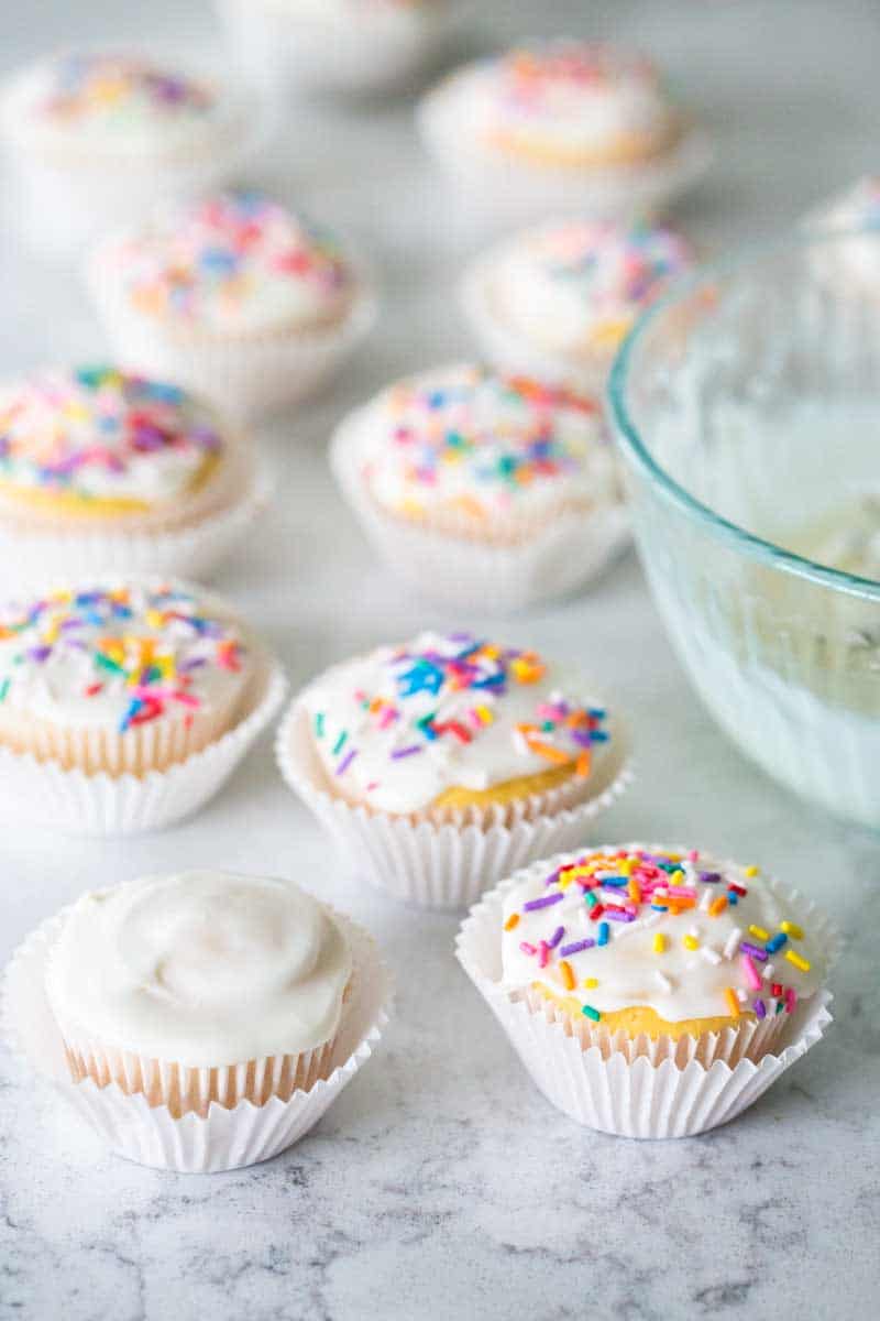 The cupcakes are lined up on the counter next to the bowl of glaze.