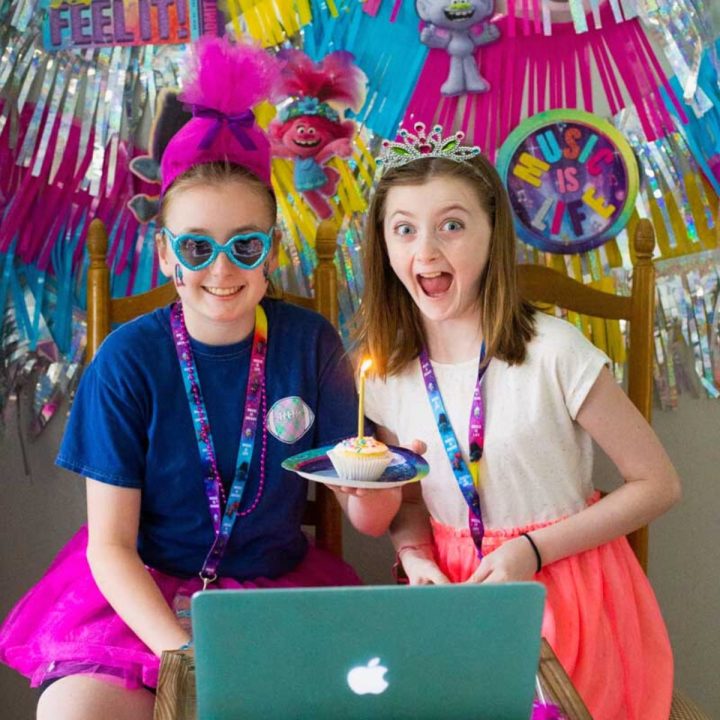 Two girls wearing party accessories in front of a laptop.
