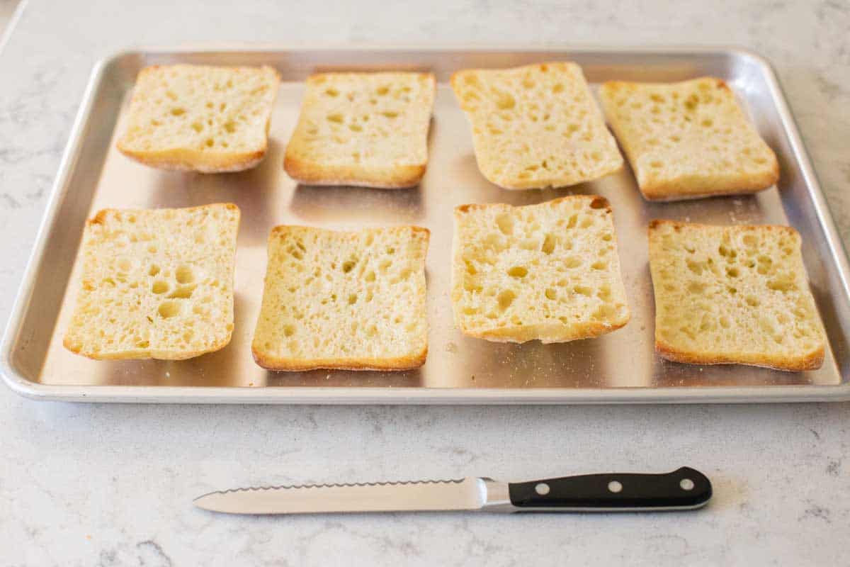 A baking pan filled with sliced ciabatta dinner rolls.