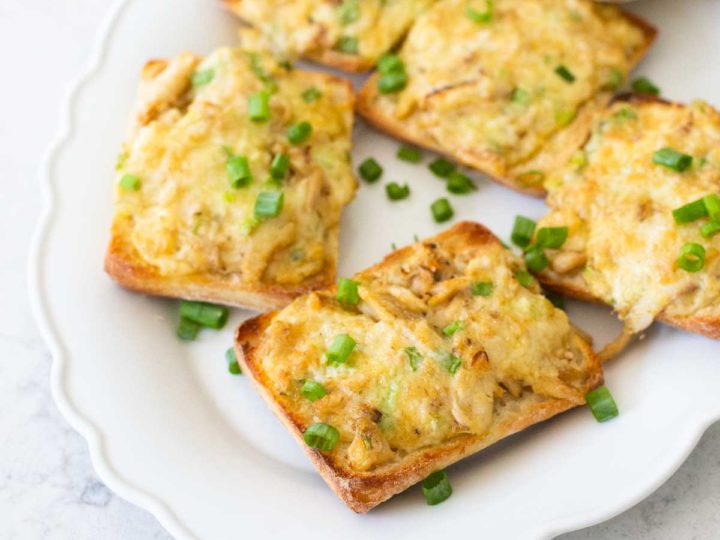 A platter of cheesy crab melts have green onions sprinkled over the top.