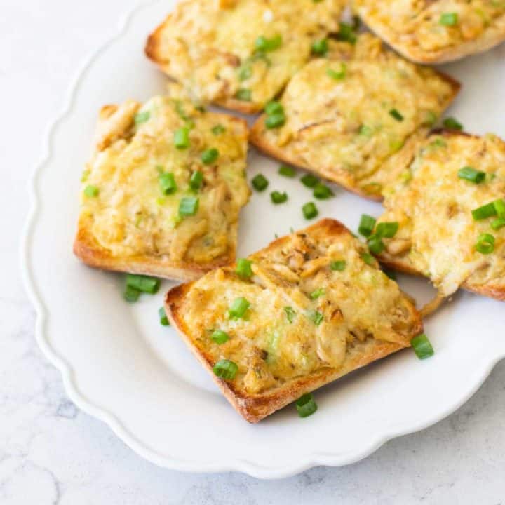 A platter of cheesy crab melts have green onions sprinkled over the top.