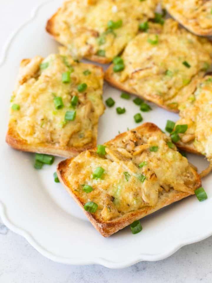 A platter of cheesy crab melts have green onions sprinkled over the top.