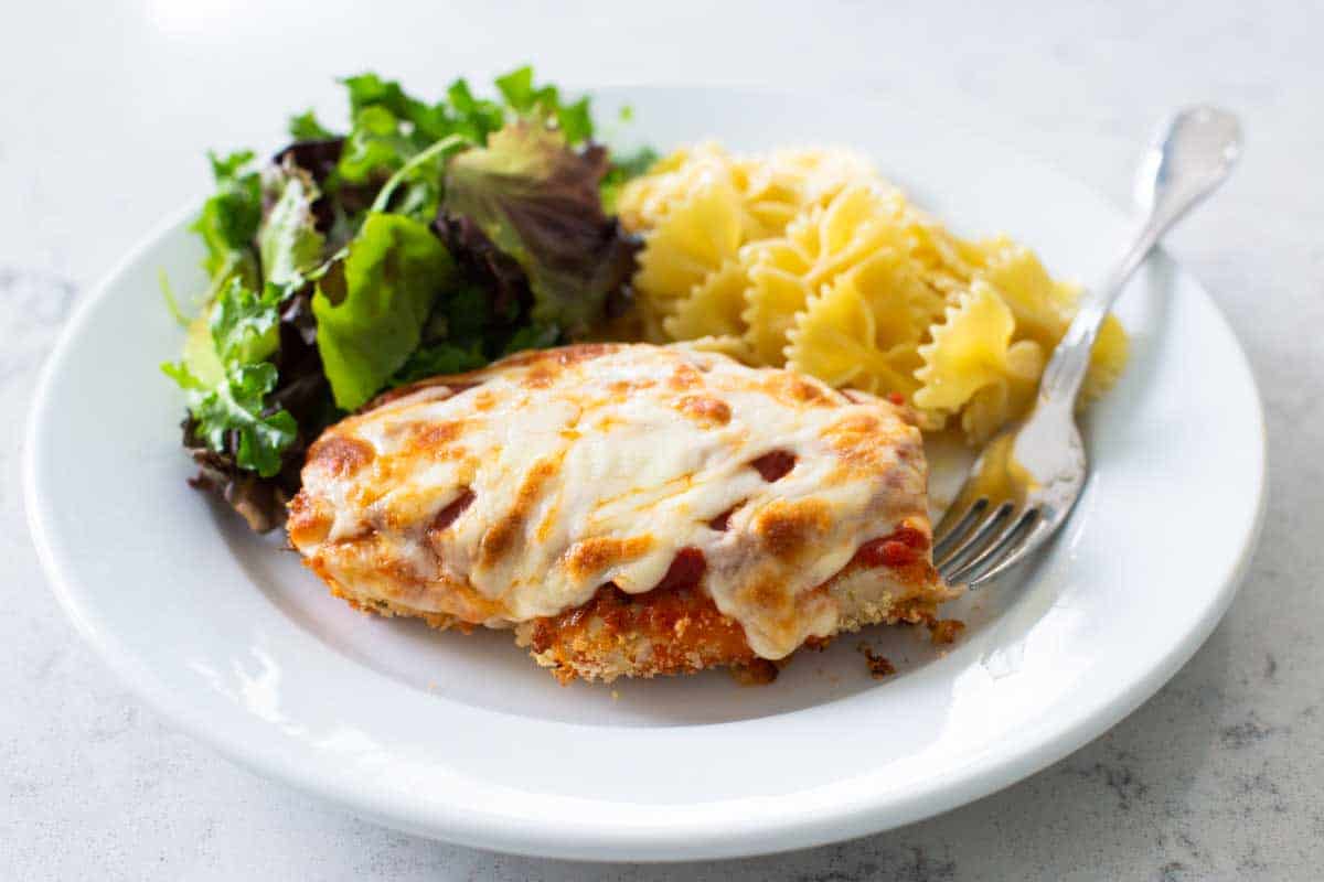 The dinner plate has the finished chicken parmesan with a green salad and buttered noodles.