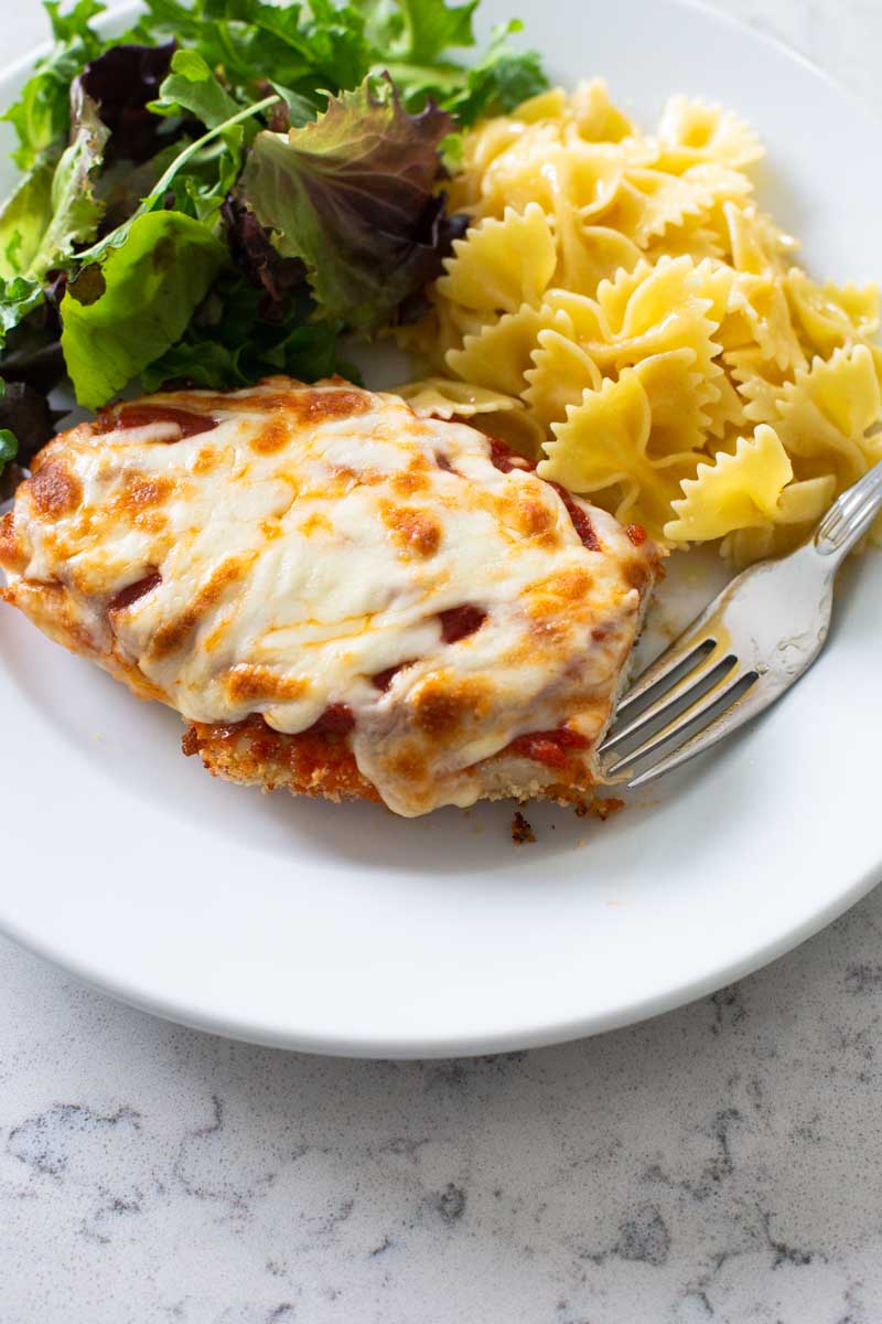 Finished chicken parmesan on a plate with one bite missing.