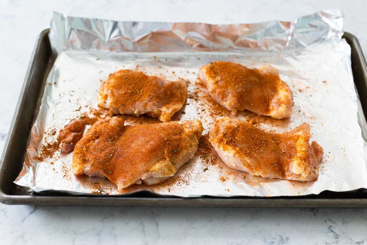 The spice has been sprinkled over the chicken thighs on a baking sheet lined with aluminum foil.