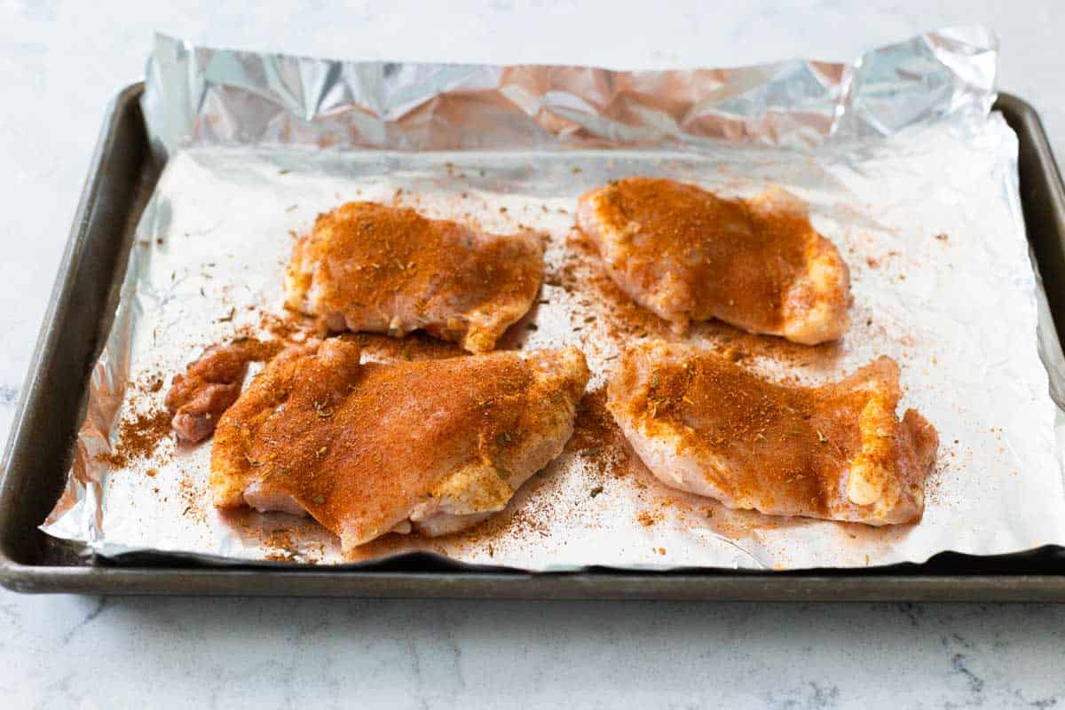 The spice has been sprinkled over the chicken thighs on a baking sheet lined with aluminum foil.