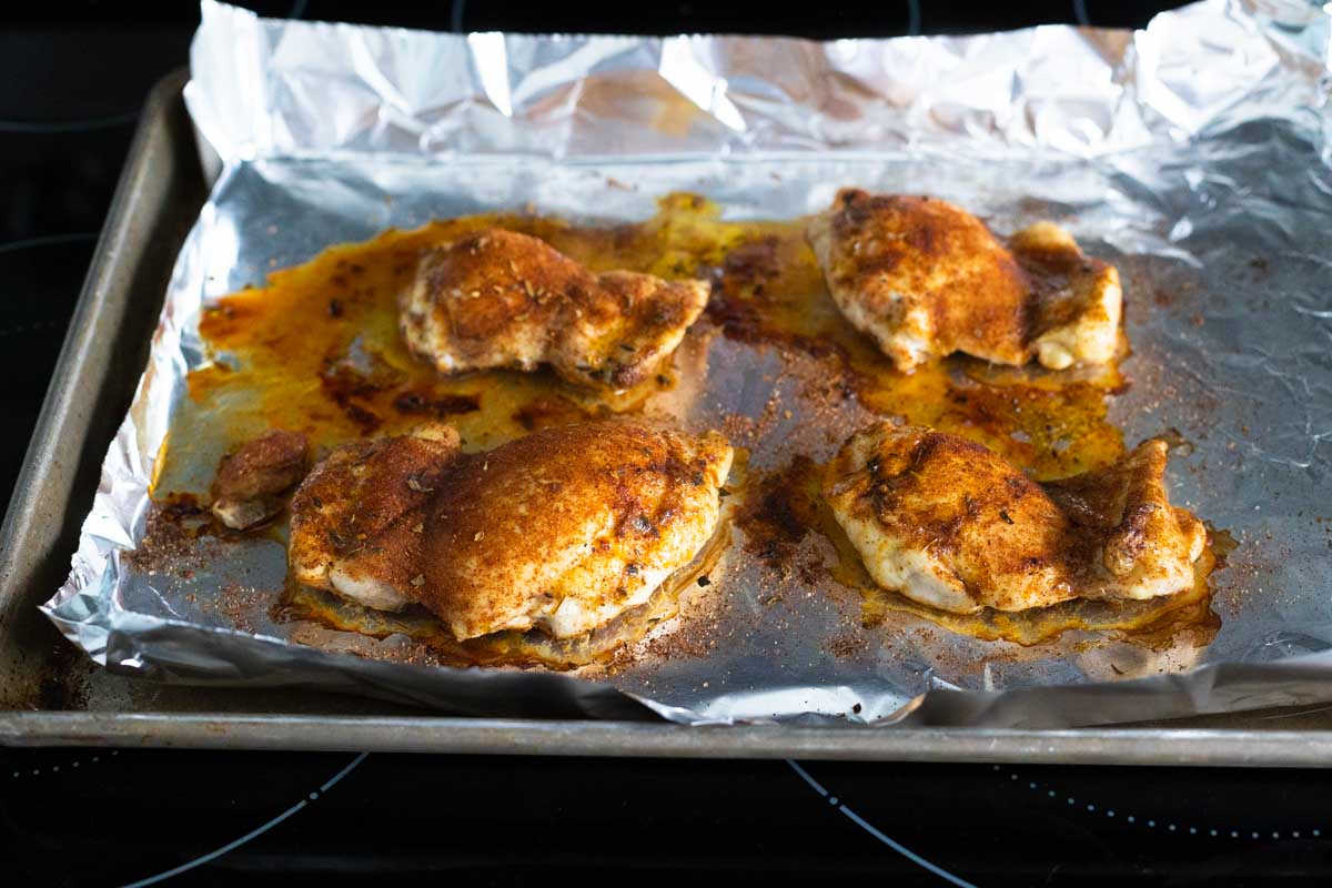 The chicken thighs have been pulled out of the oven so they can be flipped over.