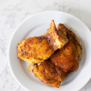 The white plate has two baked chicken thighs that have been seasoned with blackening spice.