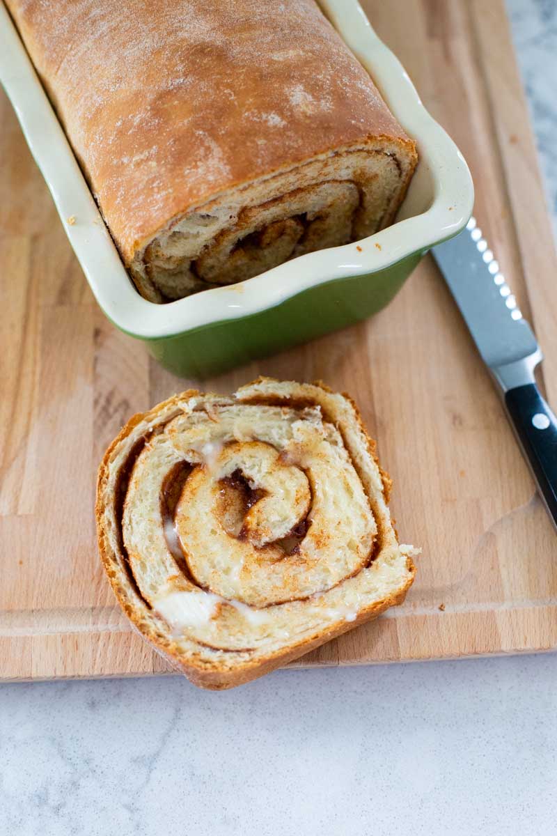 The cinnamon swirl bread slice is on the cutting board and has been slathered with butter.