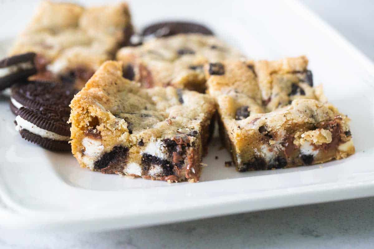 A white platter has several squares of OREO blondies next to whole OREO cookies.