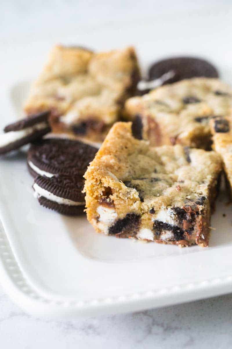 A blondie bar filled with oreo cookie chunks and chocolate chips has been sliced and served on a platter.