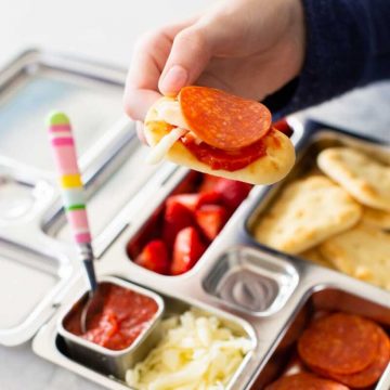 A young kid's hand is holding a homemade pizza lunchable.